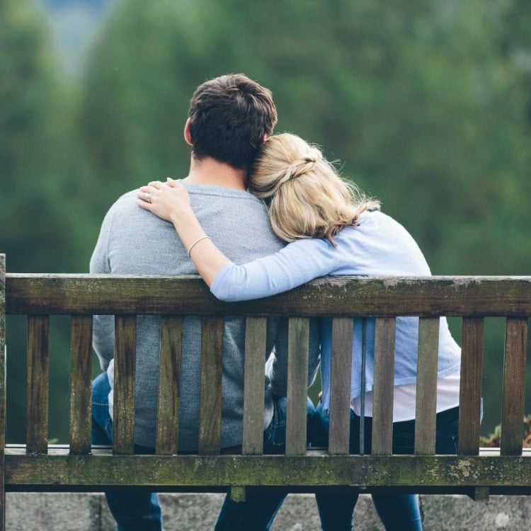 Couple on bench showing engagement ring