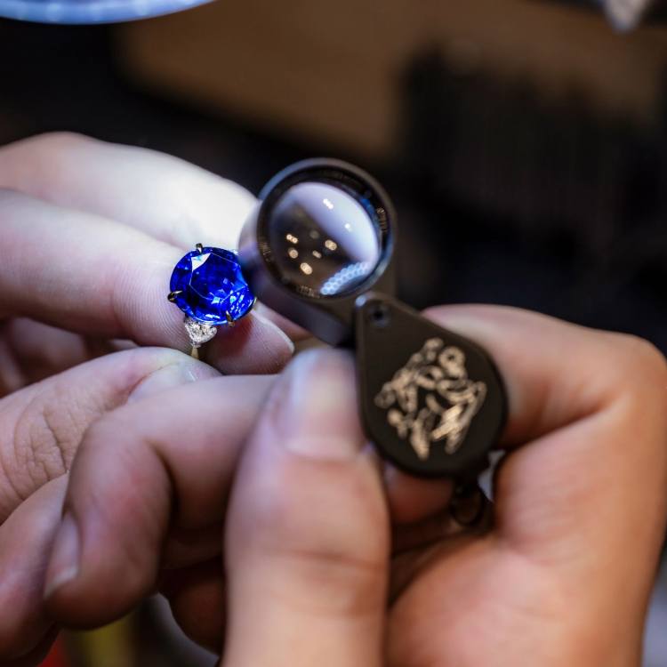 Jeweller examining a blue gemstone on a ring using a magnifying glass
